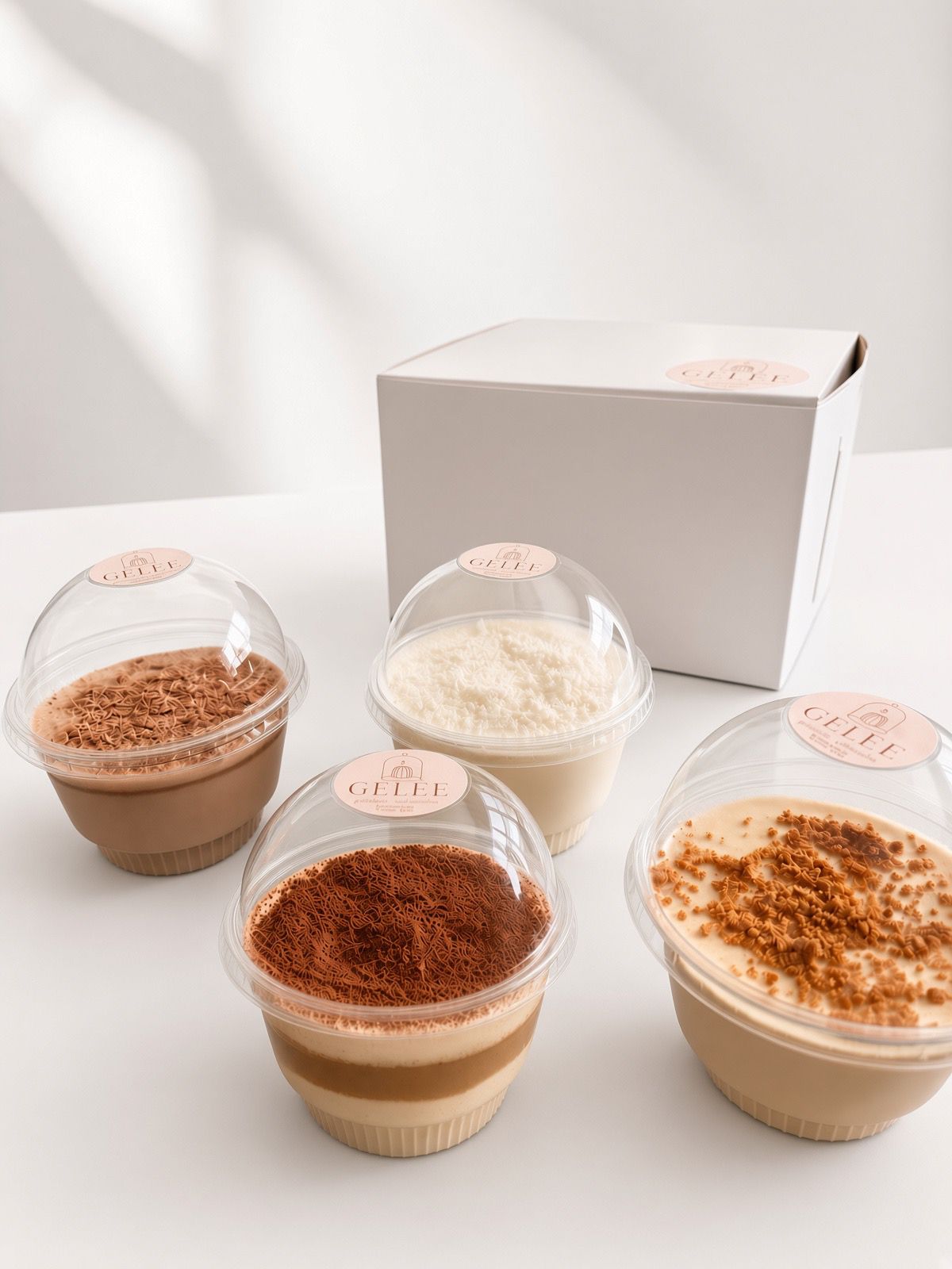 Cuatro gelatinas de GELÉE en vaso individual, con distintas coberturas, frente a la caja de la marca